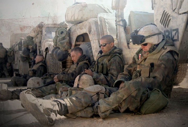 Trötta soldater vilar ut i skuggan av sina fordon.