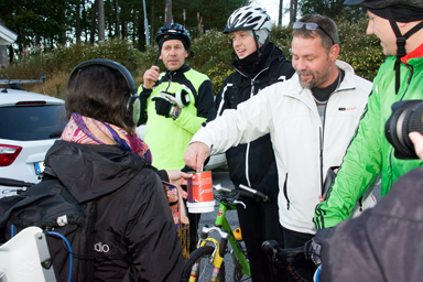 Patrik Espered stoppar i en 100-lapp i insamlingsbössan för Världens Barn.<br />De tre cyklisterna ser nöjt på.