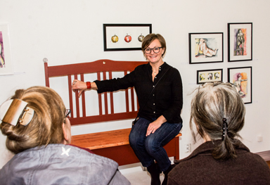 Lotta Claesson berättar för ett par besökare om soffan som hon visar på sin utställning. 